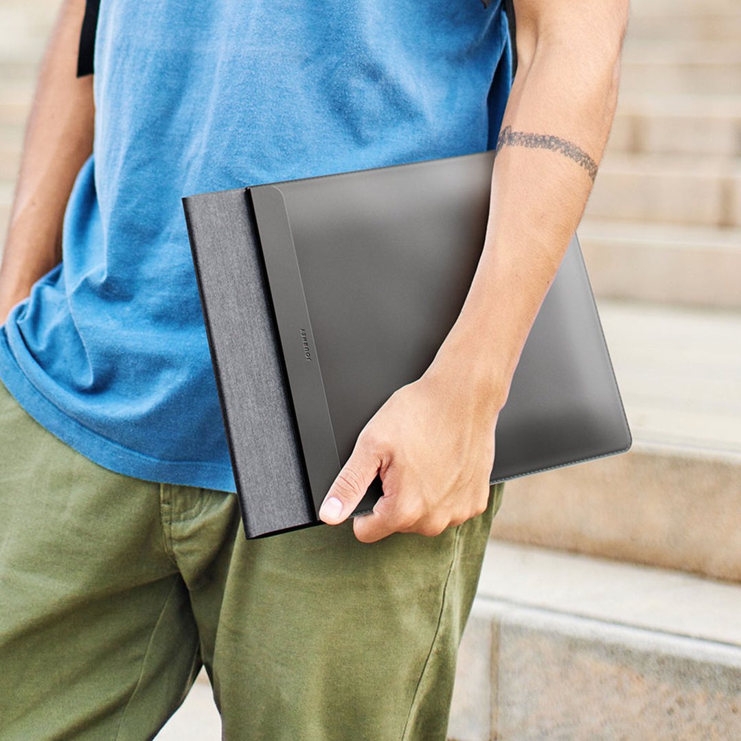 Person holding a black laptop sleeve while standing outdoors