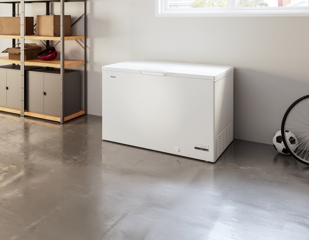 White chest freezer in a garage with shelving, boxes, and sports equipment