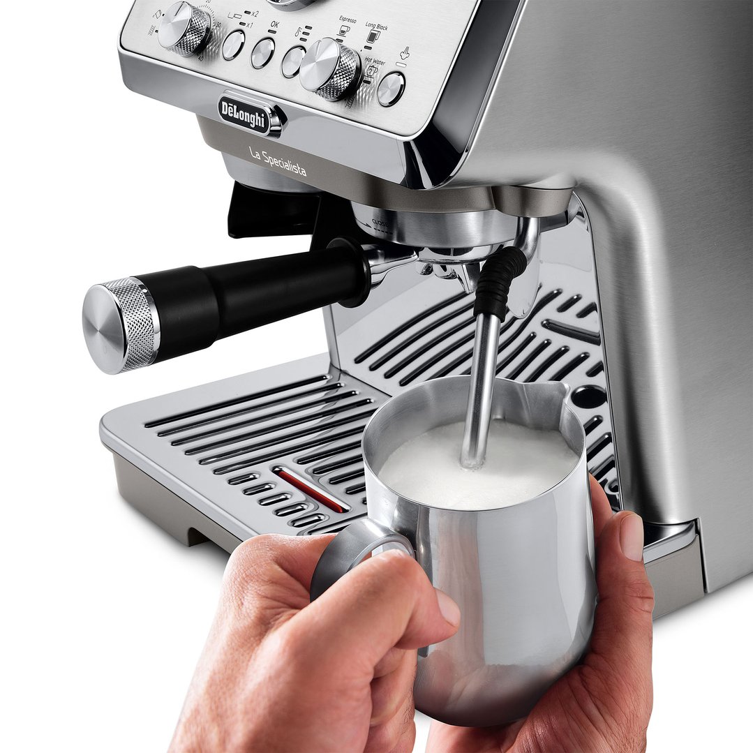 Hand holding a milk frothing jug under the steam wand of a coffee machine