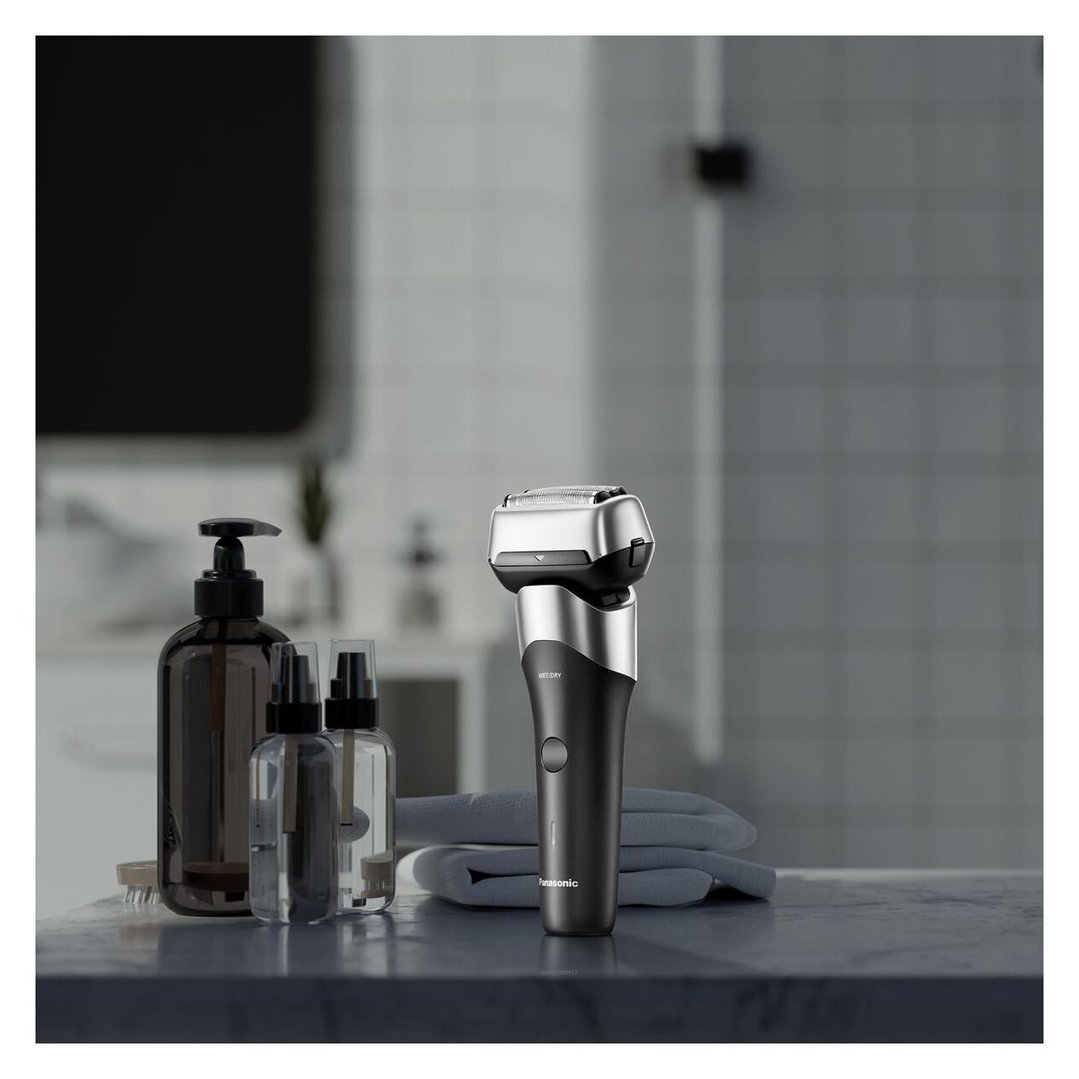 Black Panasonic electric shaver on a bathroom counter with bottles and towels