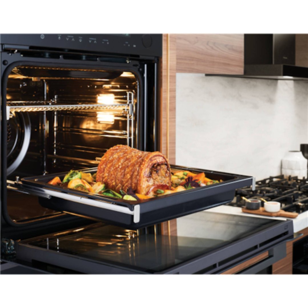 A cooked pork roast and vegetables on a tray being pulled from an oven