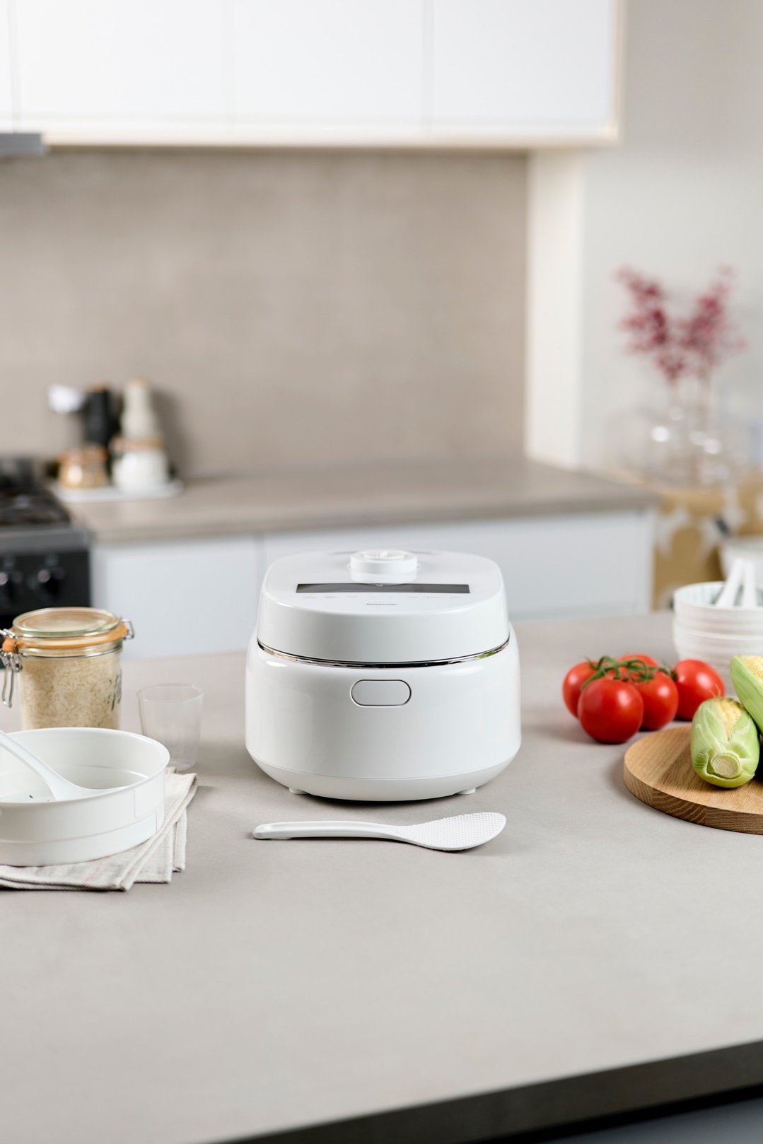 White Panasonic rice cooker on a kitchen counter with ingredients and utensils