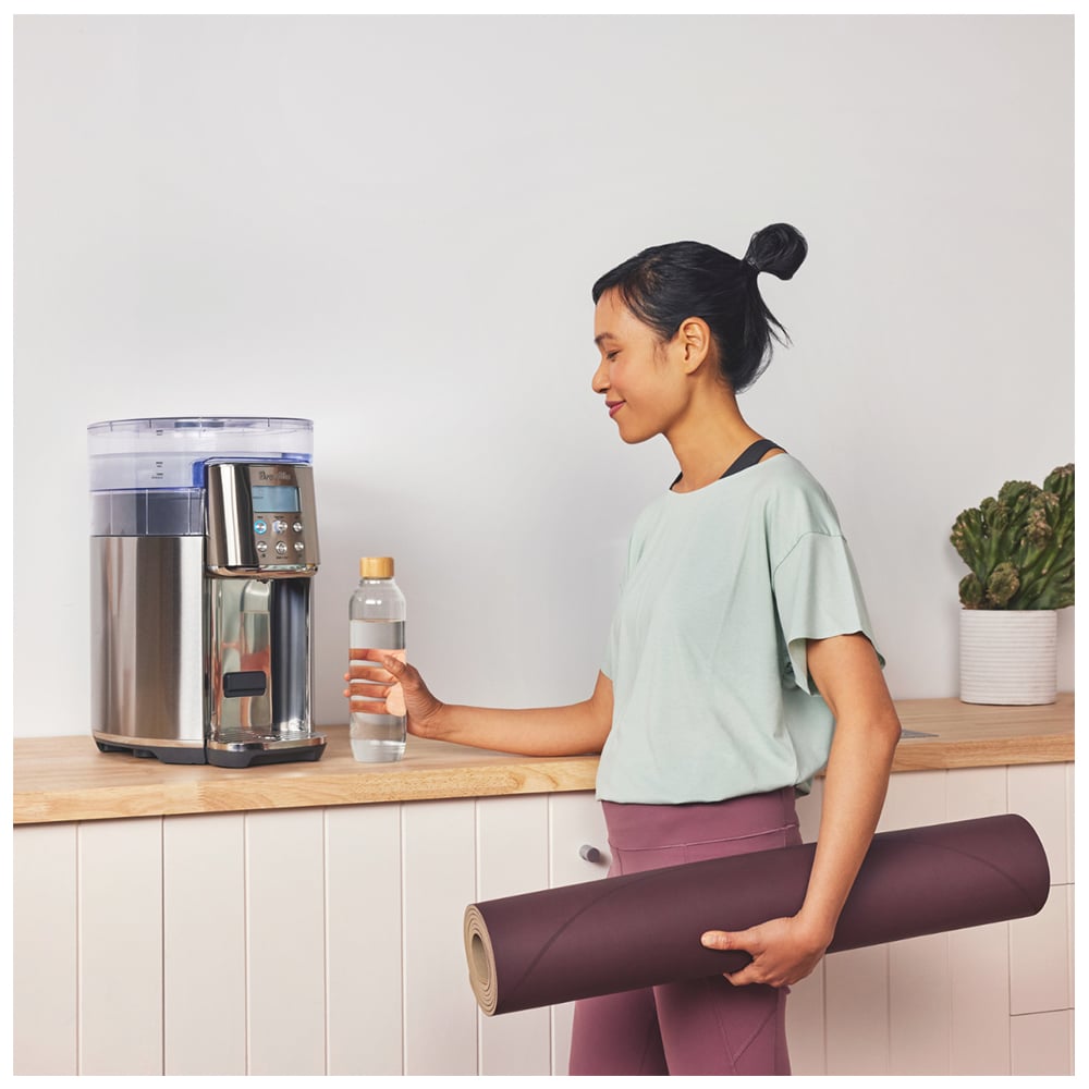 Woman filling a water bottle from a Breville AquaStation on a kitchen counter