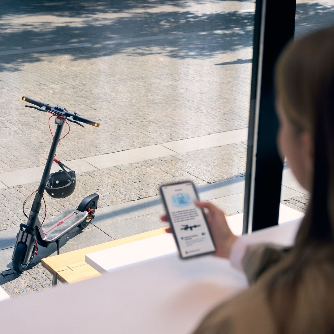 Woman using a smartphone to control an electric kickscooter parked outside a cafe