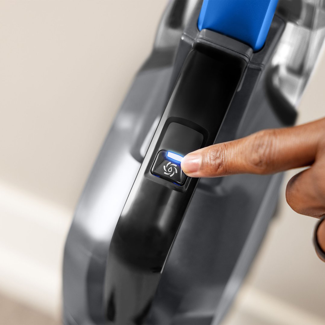 A hand pressing the power button on a BISSELL CrossWave HydroSteam vacuum cleaner