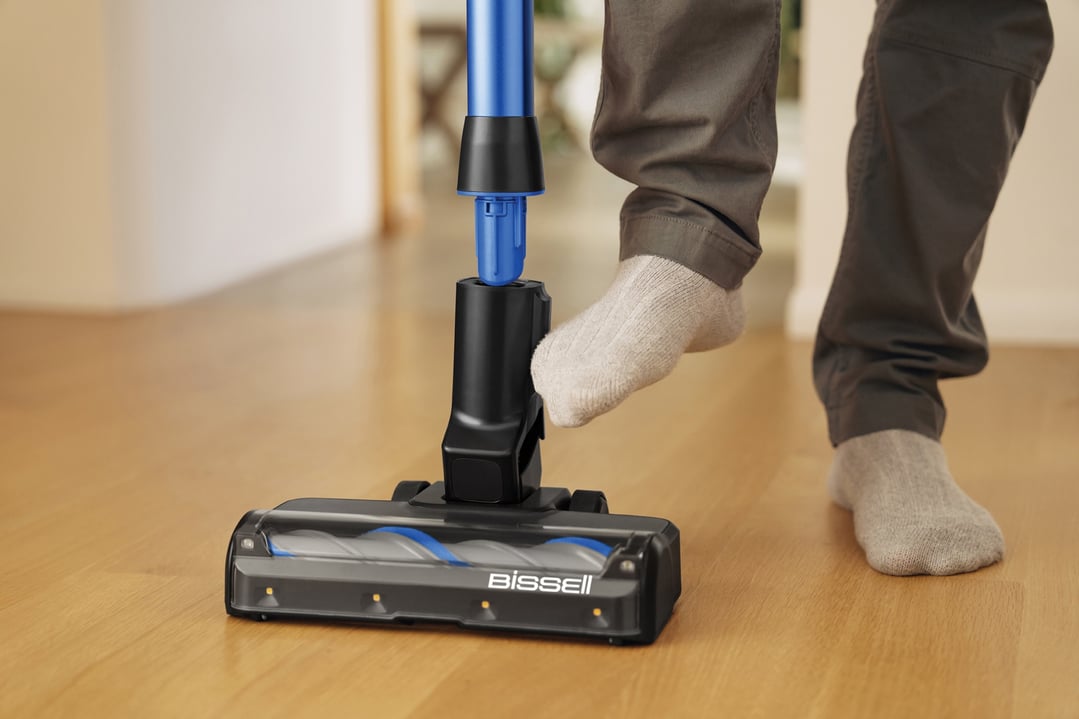Person's foot pressing down on a BISSELL handstick vacuum on a wooden floor