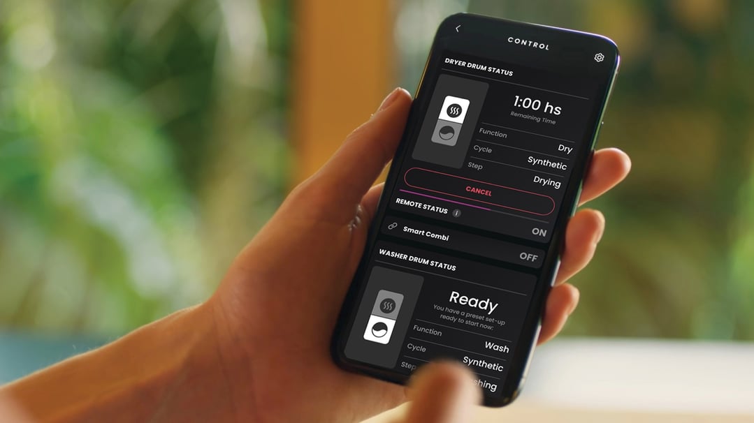 Hand holding a smartphone displaying a washer dryer combo control app