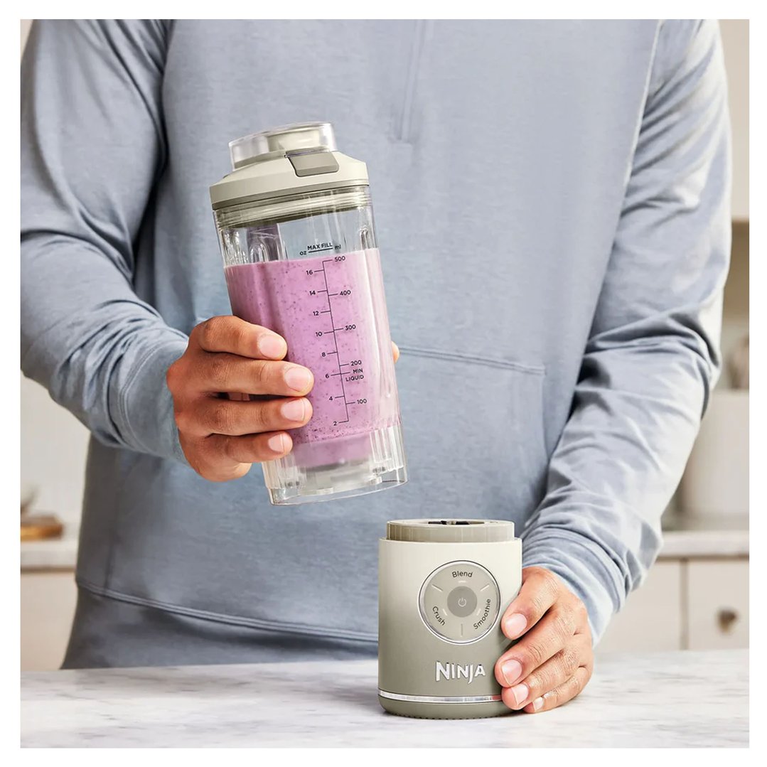 Person holding a portable blender with a purple smoothie over its base