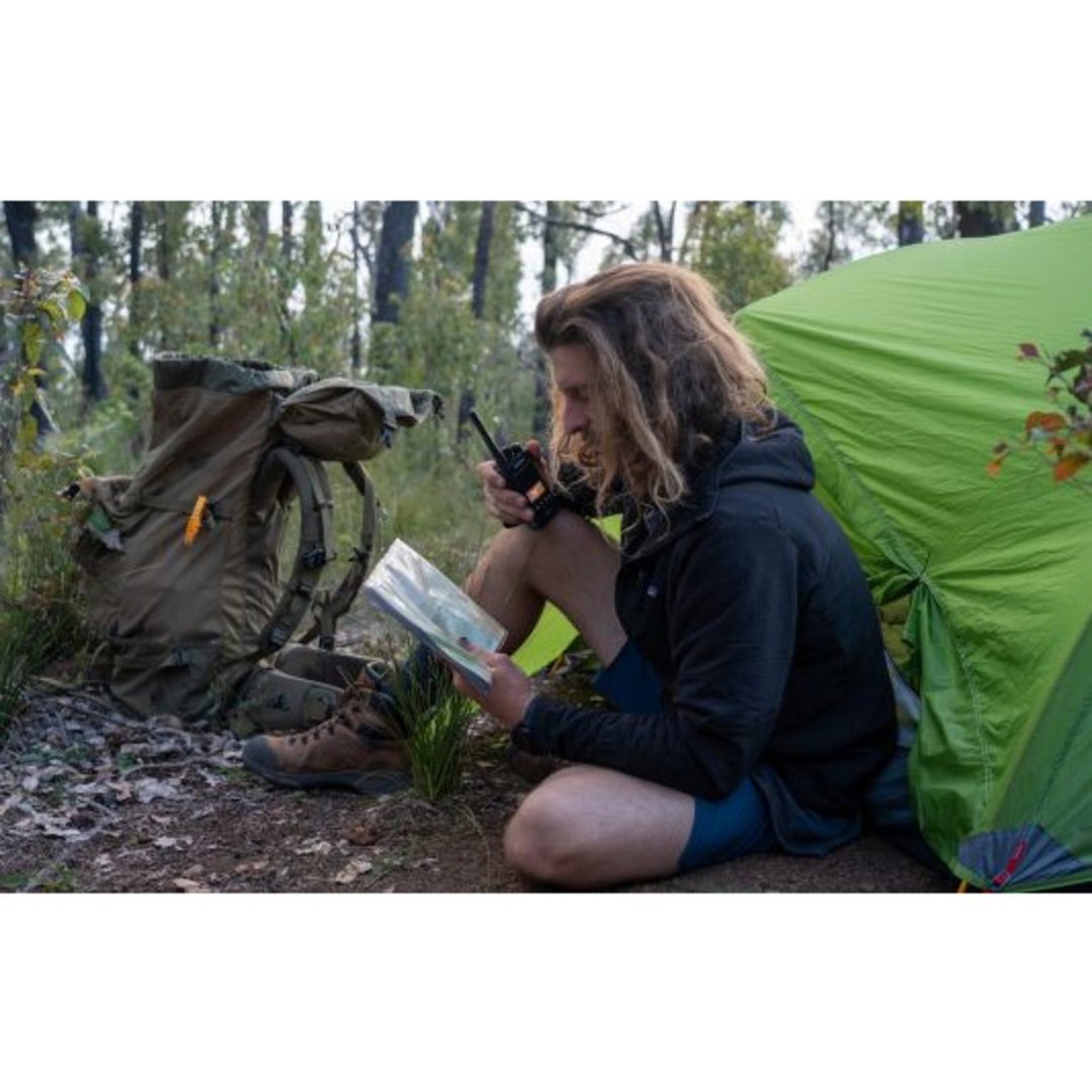 Man holding a UHF CB handheld radio and map next to a tent and backpack