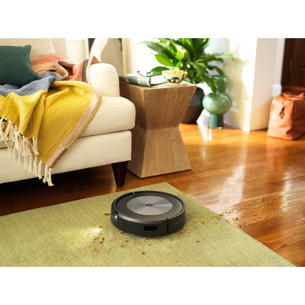 Roomba j7+ robot vacuum cleaning colorful debris from a green rug in a living room
