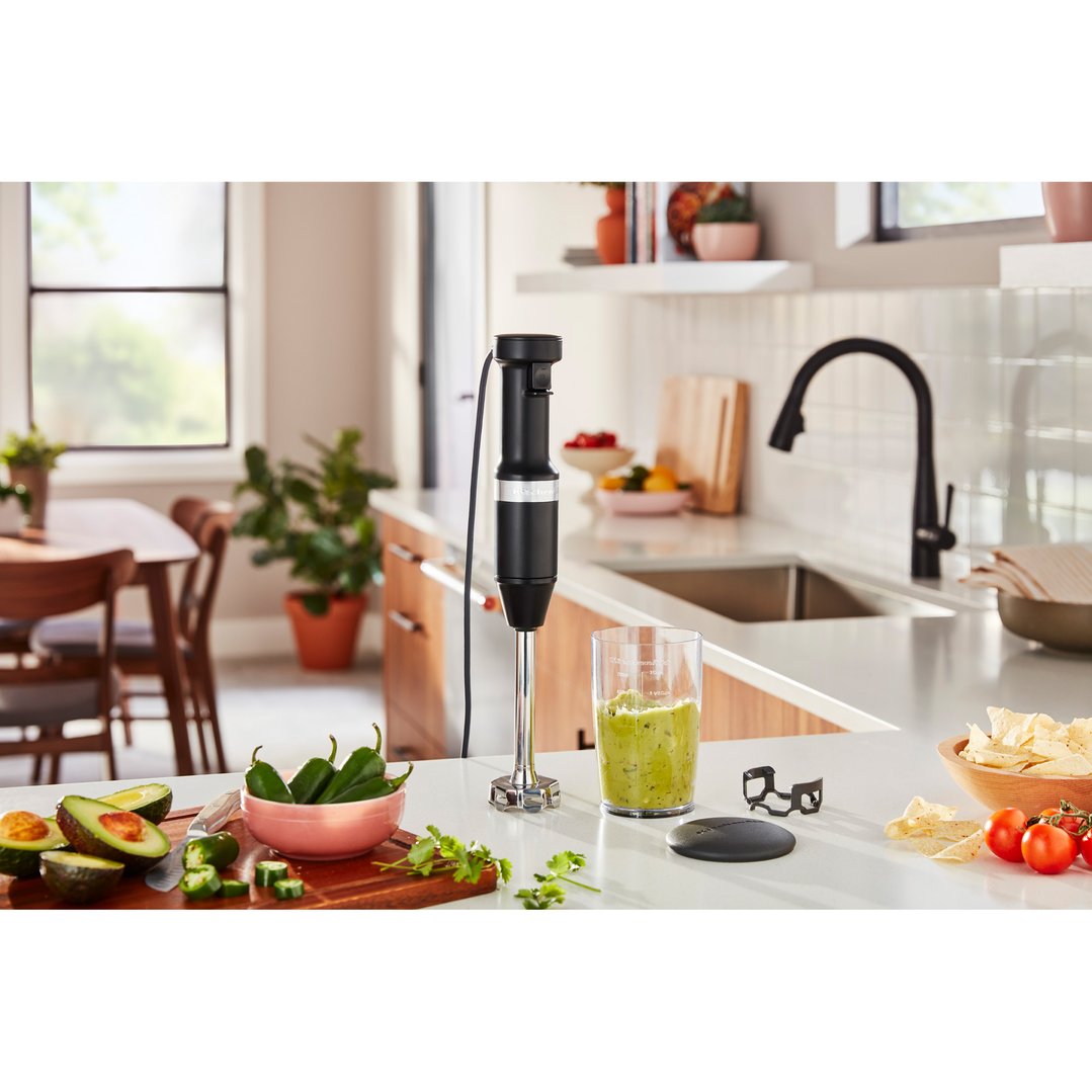 Black KitchenAid stick blender making guacamole on a kitchen counter