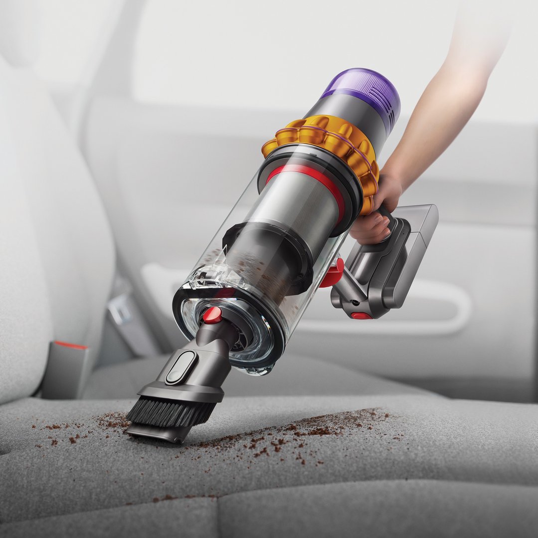 Hand using a Dyson handStickVacuum to clean dirt from a car seat