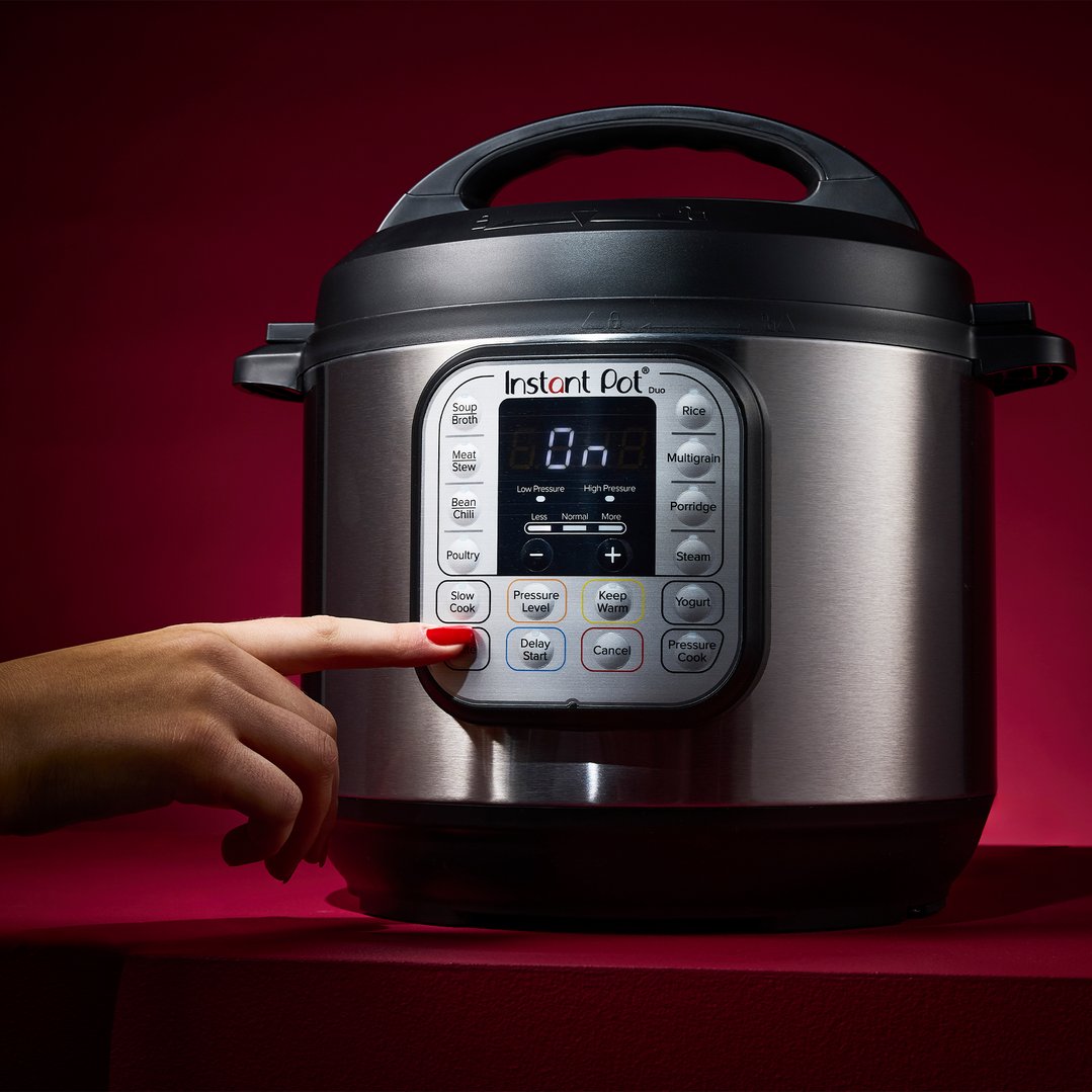 A hand presses a button on the control panel of an Instant Pot multi-cooker