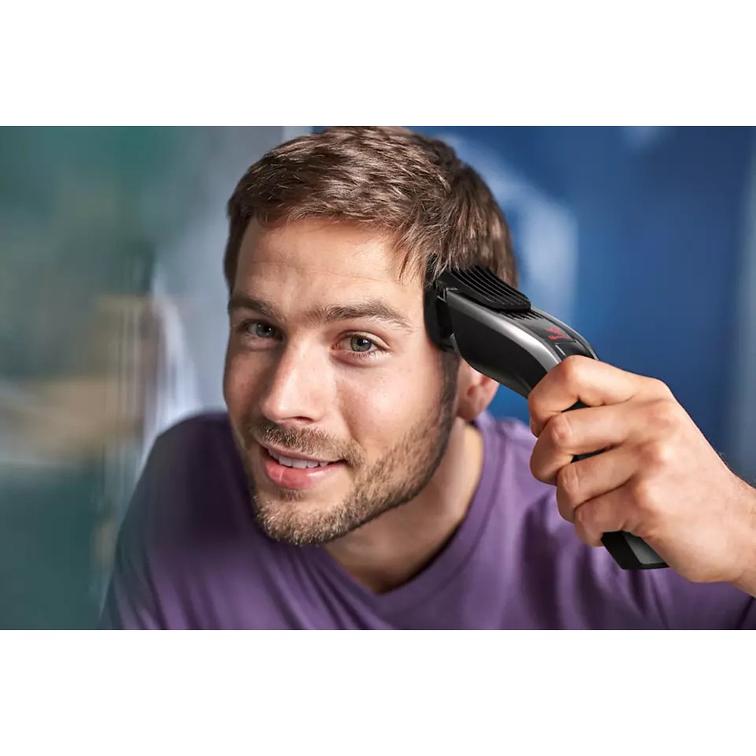 Man using a hair clipper to trim his hair, looking at the camera