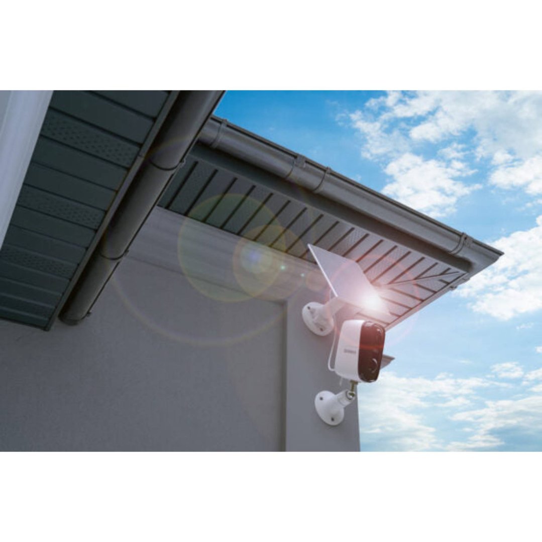 Solar panel and security camera mounted on a building under a blue sky