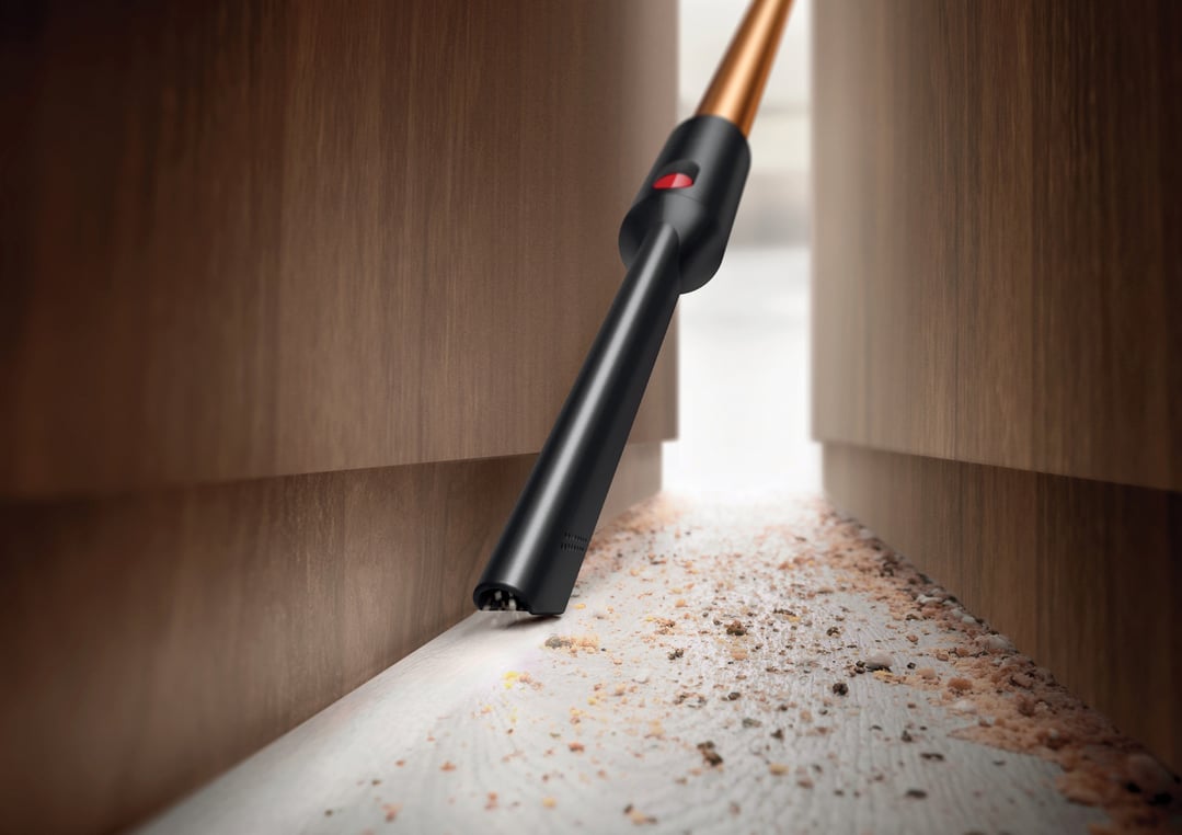 Handheld vacuum cleaning debris from a narrow gap between wooden cabinets