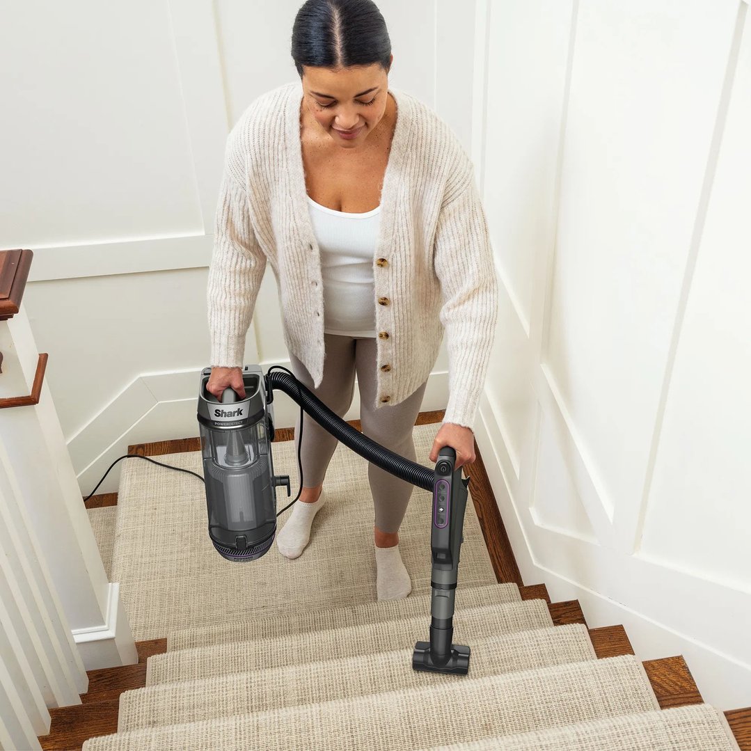 Woman vacuuming carpeted stairs with a Shark PowerDetect corded upright vacuum cleaner