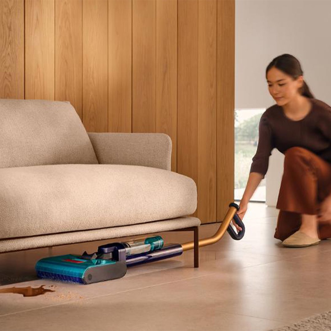 Woman using a Dyson vacuum cleaner to clean spills under a sofa