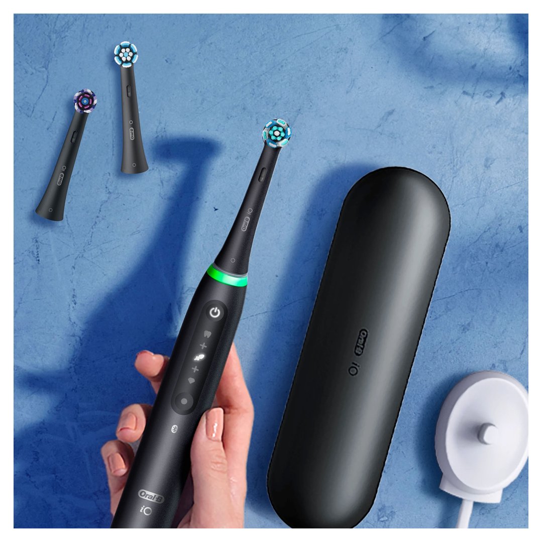 Hand holding a black electric toothbrush with accessories on a blue surface