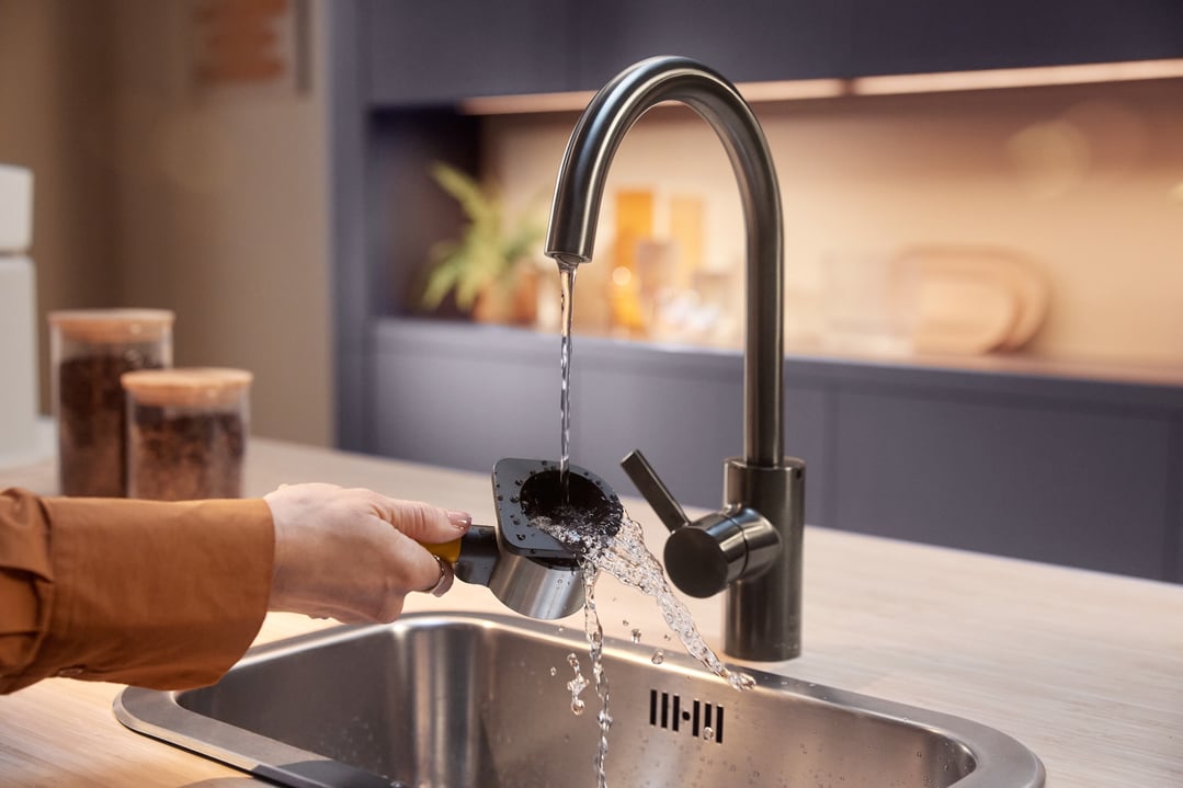 Person rinsing a portafilter under a kitchen faucet in a modern kitchen