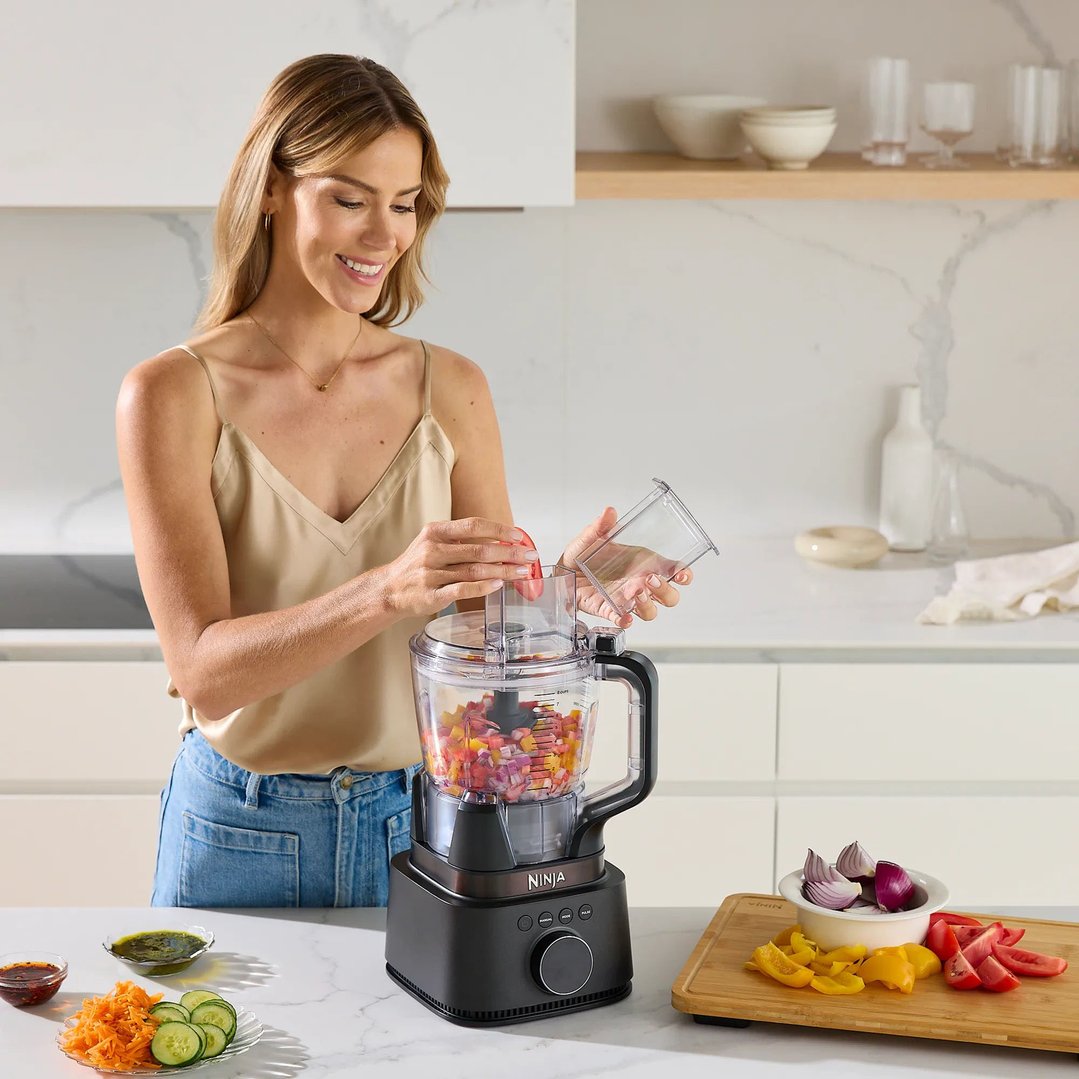 Woman adding ingredients to a Ninja blender in a modern kitchen