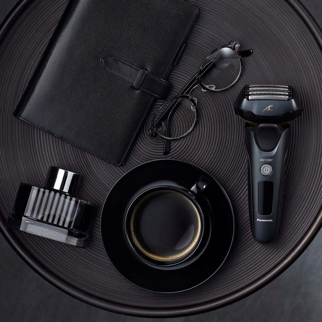 Panasonic shaver, glasses, notebook, coffee cup, and cologne on a dark table
