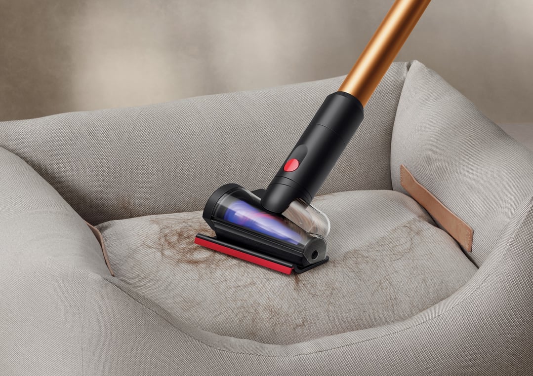 DYSON handStickVacuum cleaning pet hair from a light grey pet bed