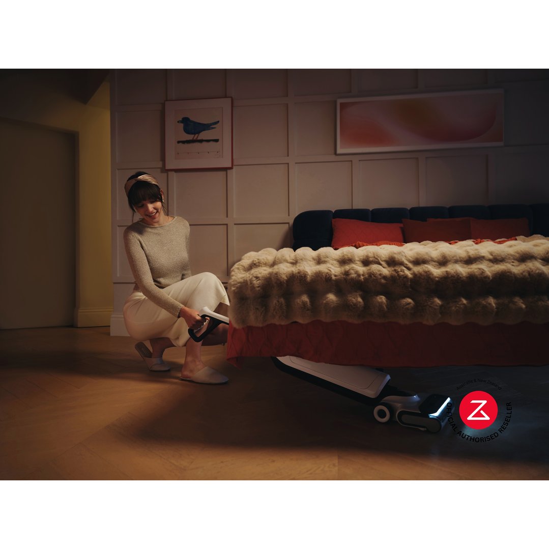 Woman using a white vacuum cleaner to clean under a bed in a bedroom