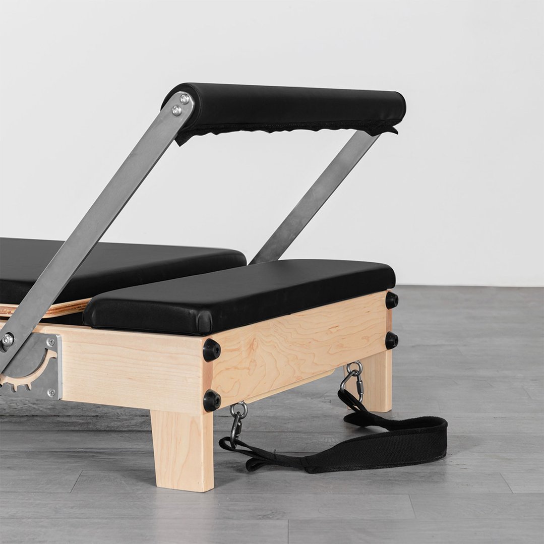 Pilates reformer machine with black padding and wooden frame on a grey floor