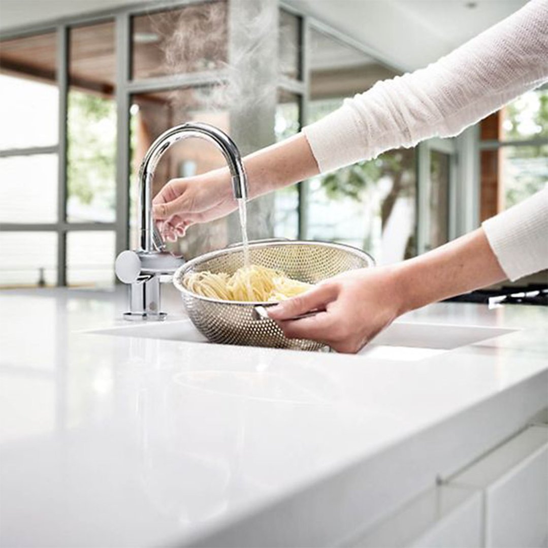 Hands rinsing pasta in a colander under a chrome hot and cold water tap