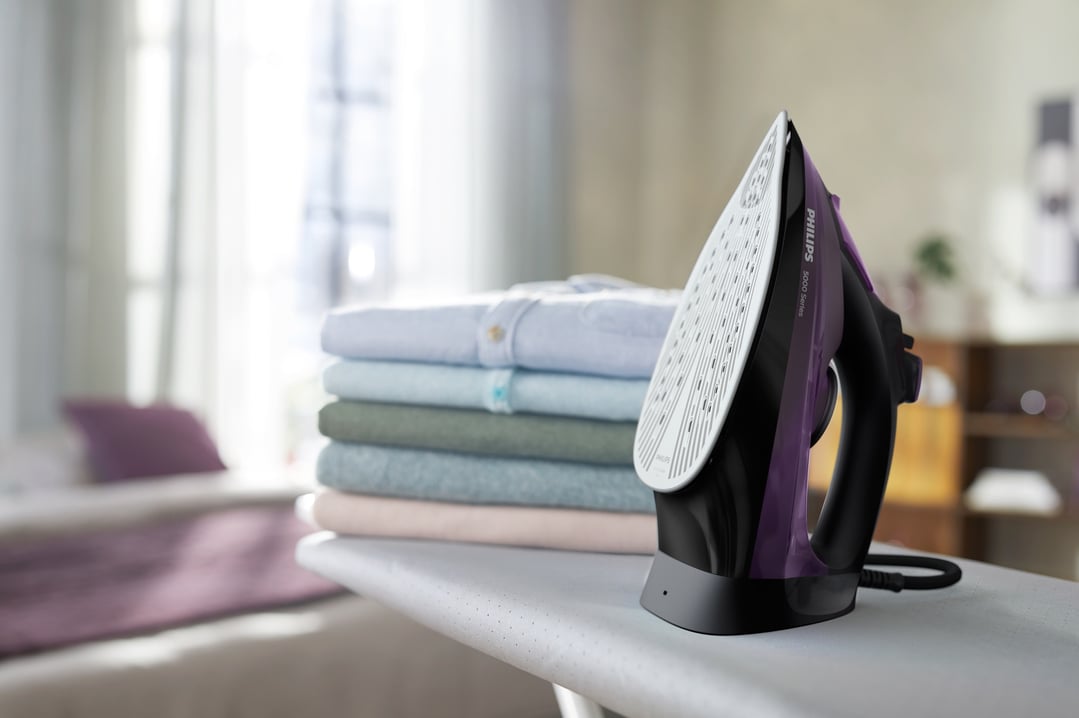 Philips steam iron on an ironing board with a stack of folded clothes