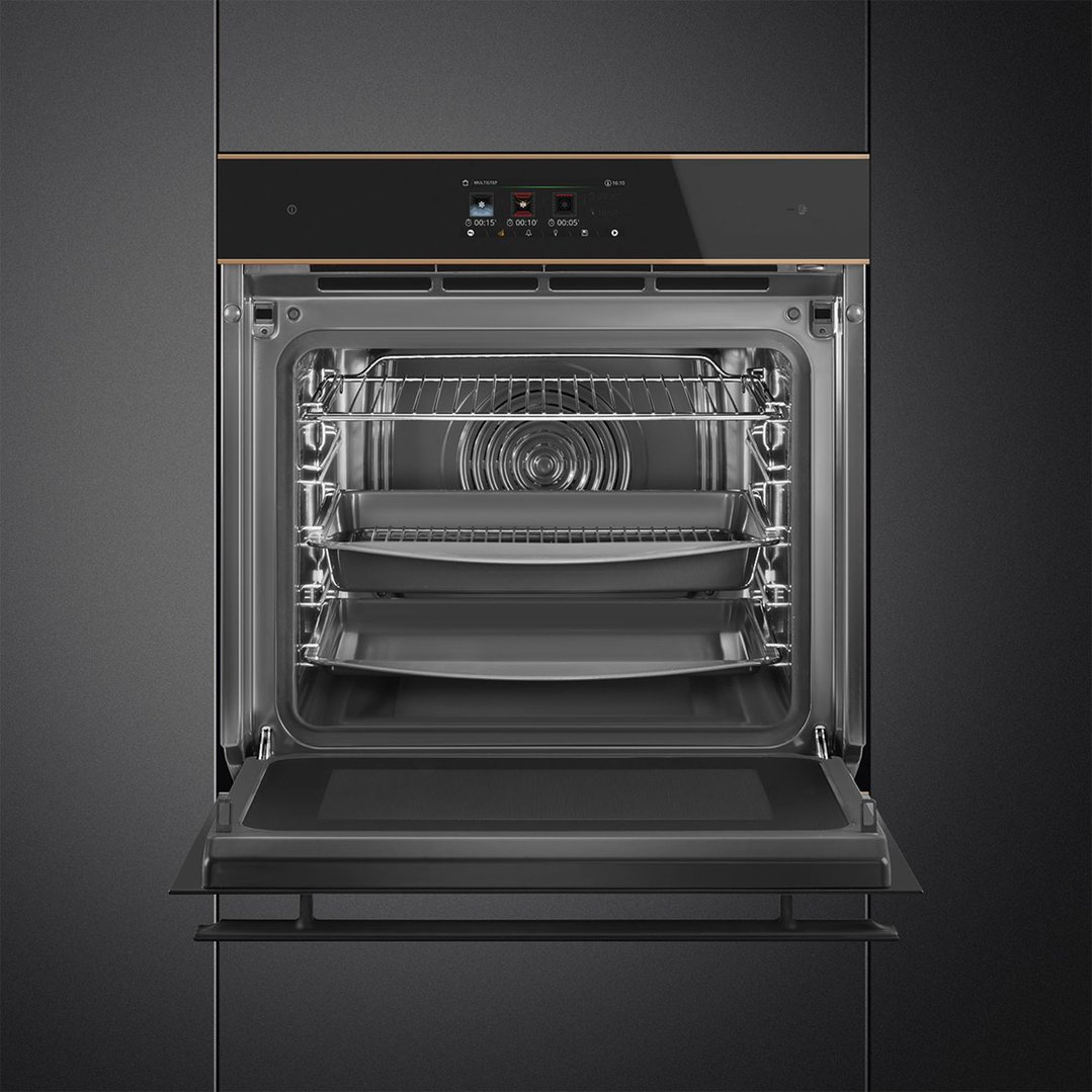An open black oven with copper trim built into dark cabinetry