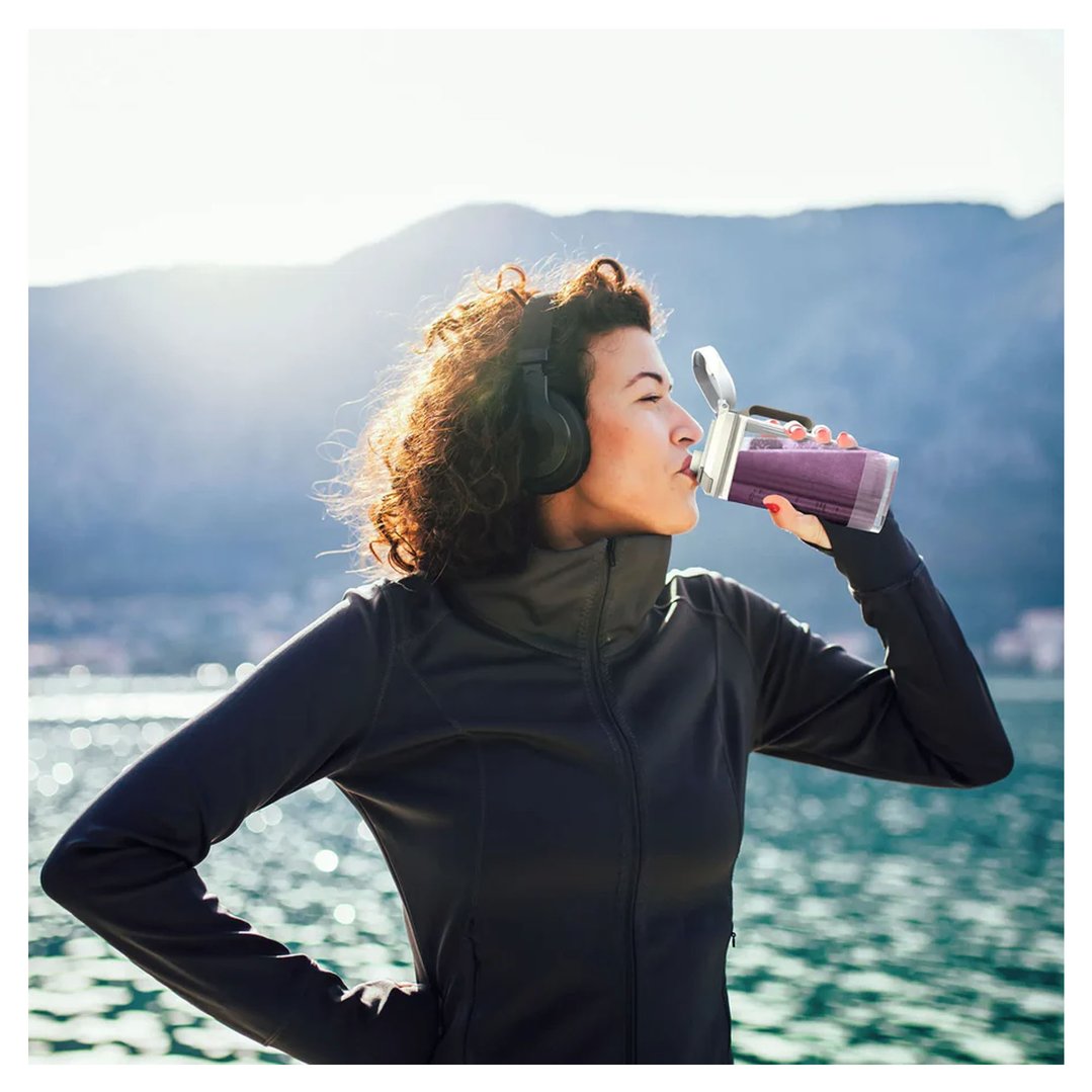 Woman wearing headphones drinking from a Ninja Blast portable blender outdoors