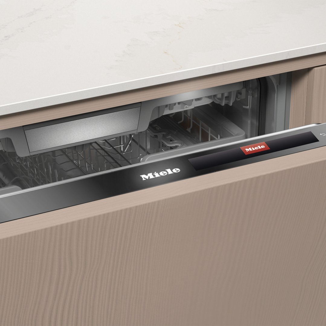 Partially open integrated Miele dishwasher with a light wood panel and white countertop