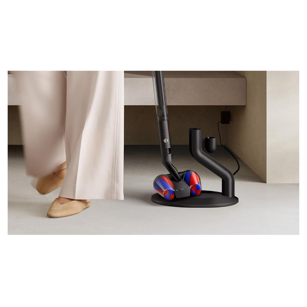 DYSON PencilVac Fluffycones Cleaner charging on its stand with a person nearby