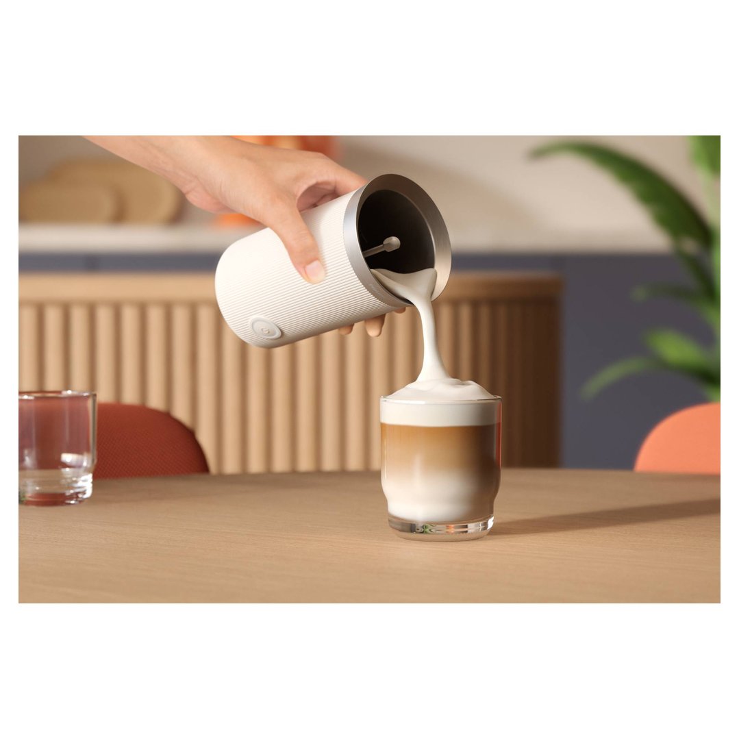 Hand pouring frothed milk from a PHILIPS Baristina Milk Frother into a glass