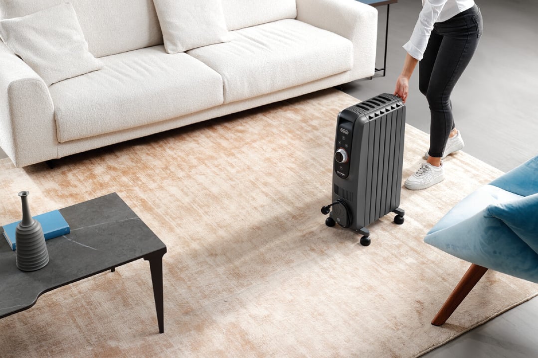 Woman moving a black oil column heater on wheels in a living room