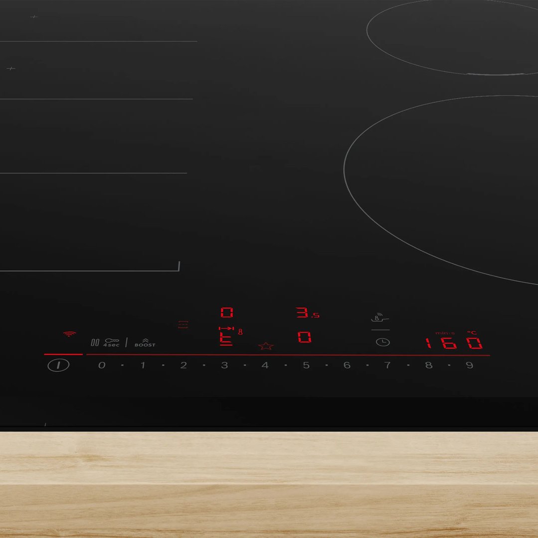 Close-up of a black induction cooktop with red digital controls on a wooden surface
