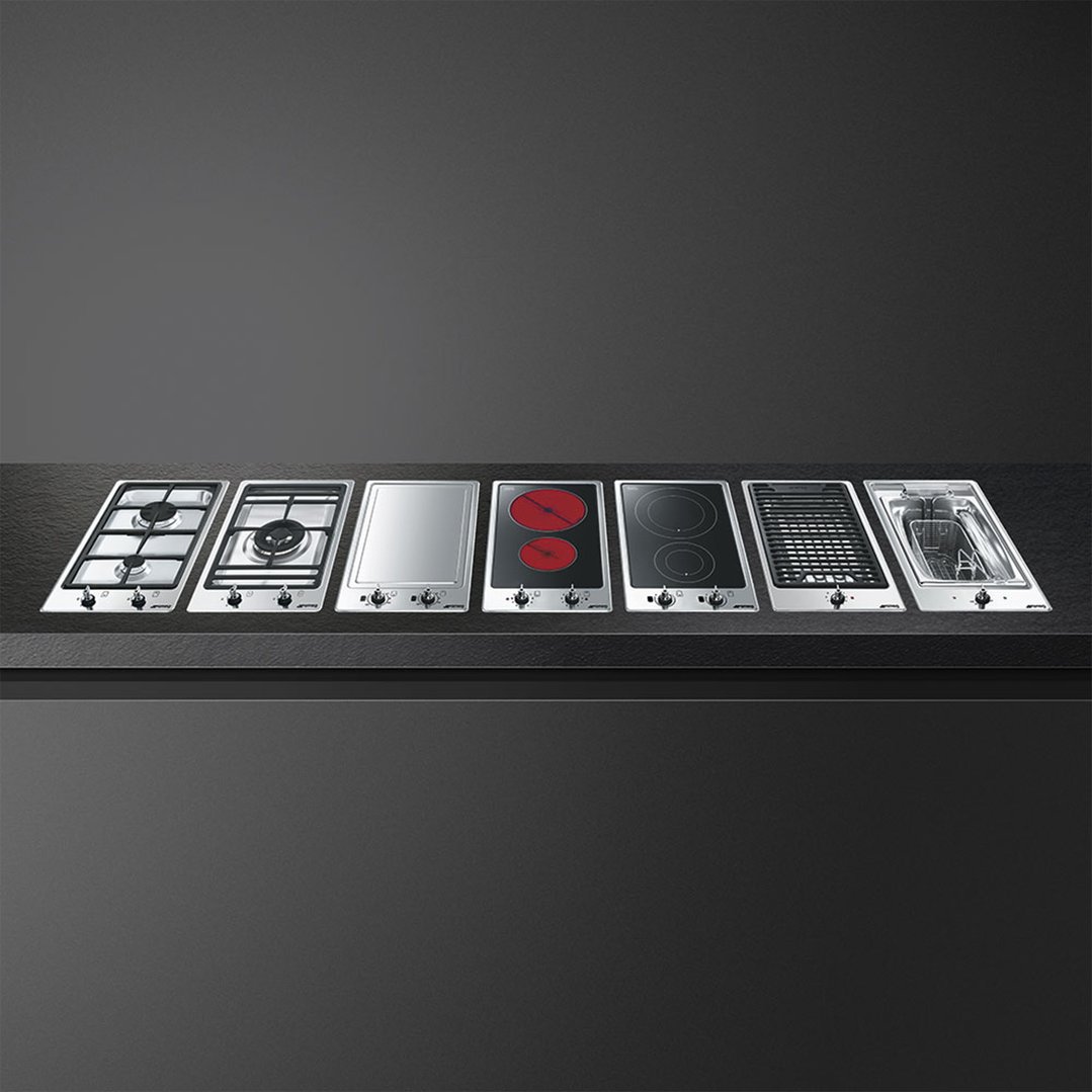 Seven different cooktops, including a fryer hob, arranged on a dark countertop