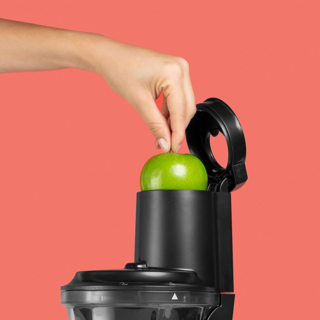 Hand placing a green apple into the top of a black Nutribullet Slow Juicer