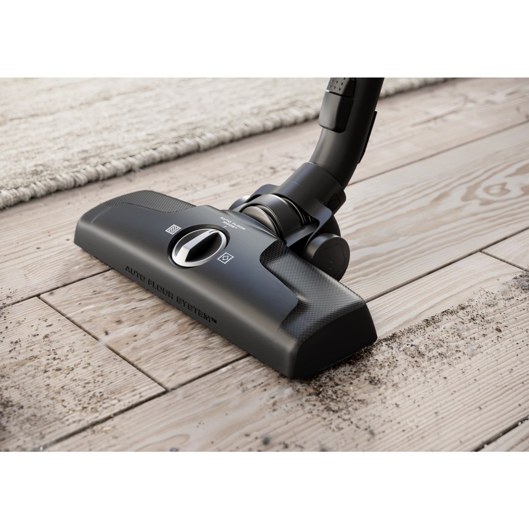 Vacuum cleaner head on a wooden floor with dirt next to a rug