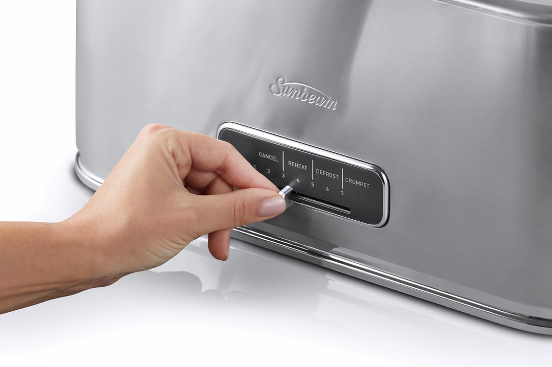 A hand adjusting the browning control on a stainless steel Sunbeam toaster