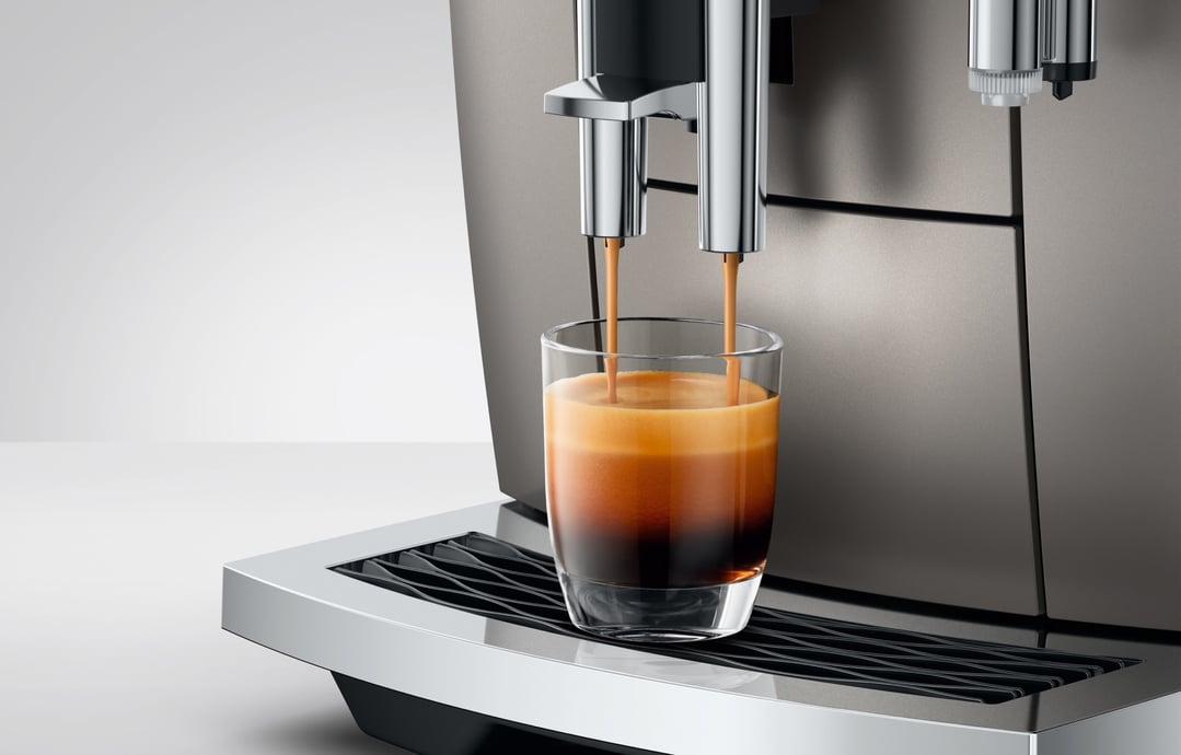 Coffee machine dispensing espresso into a glass on a neutral background