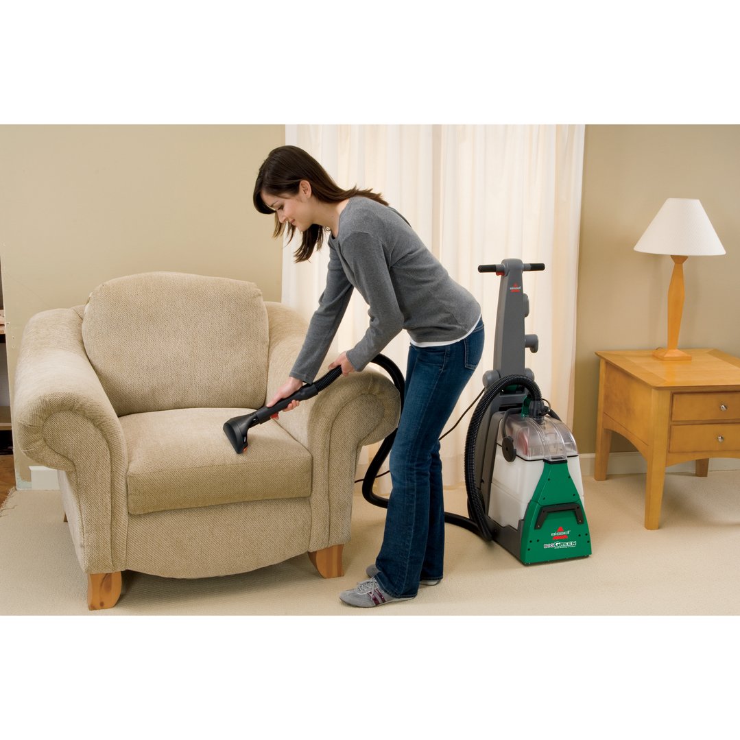 Woman deep cleaning a beige armchair with a BISSELL Big Green vacuum cleaner