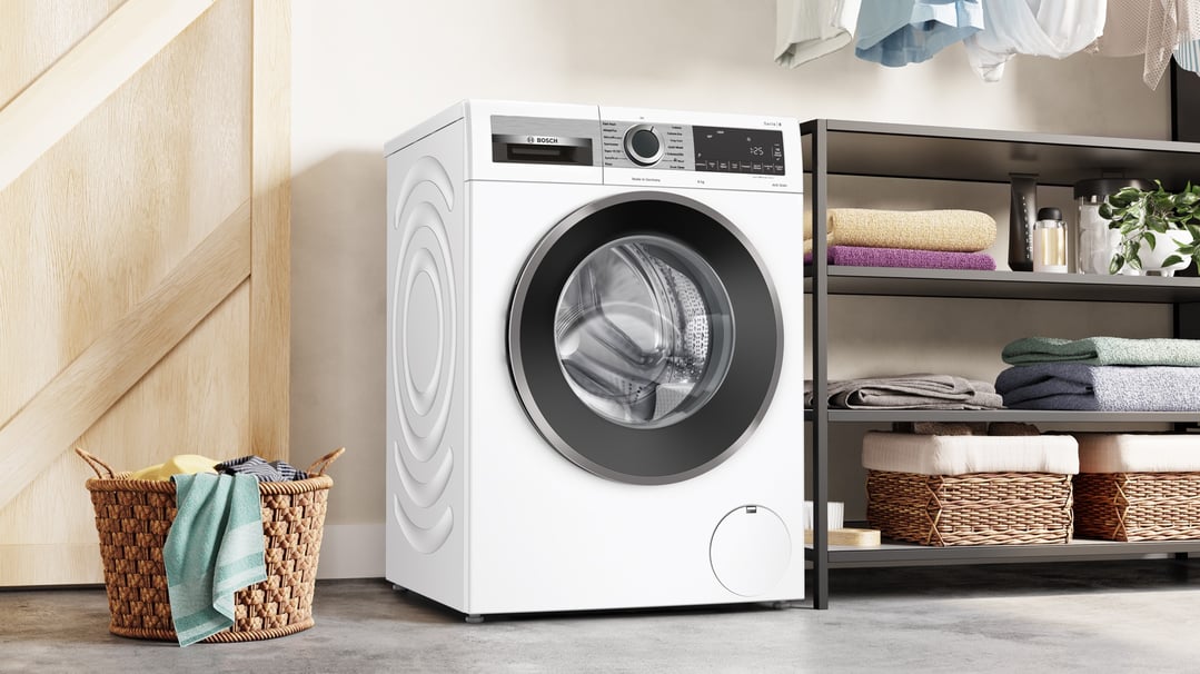 White Bosch washing machine in a laundry room with a basket and shelves