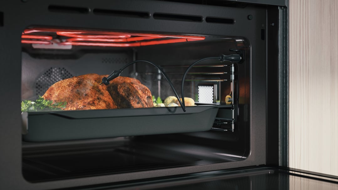 Roasted chicken and vegetables cooking inside a microwave oven with probes