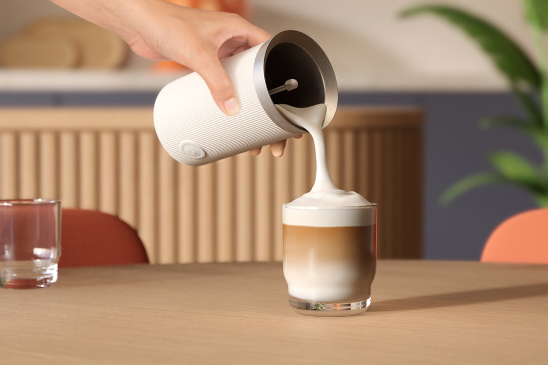 Hand pouring frothed milk from a Philips milk frother into a glass