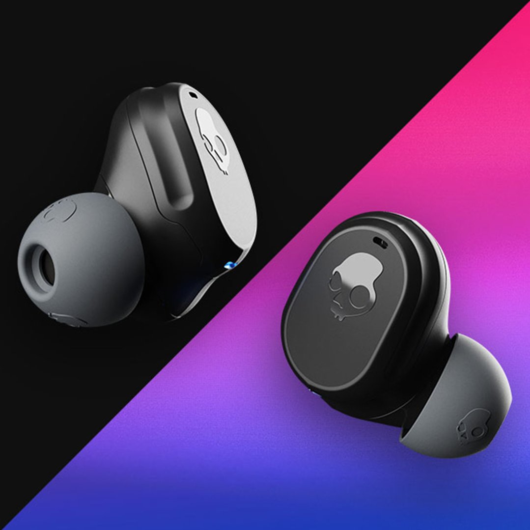 Two black Skullcandy earbuds with gray tips on a split black and gradient background