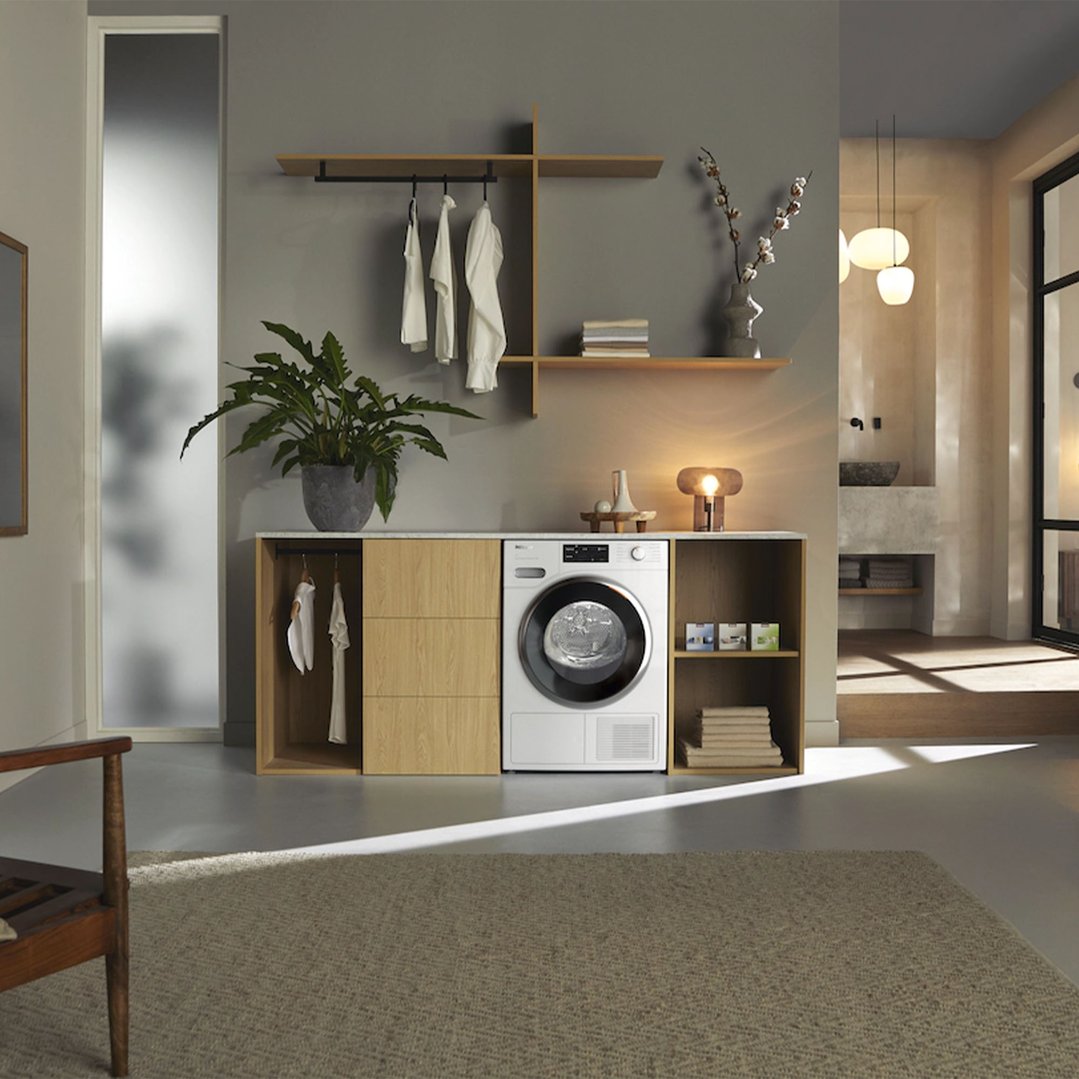 White heat pump dryer integrated into wooden cabinetry in a modern laundry room