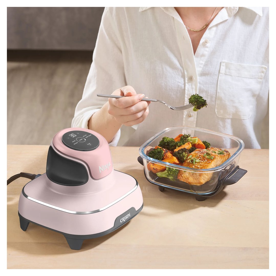 Woman eating salmon and vegetables from a glass container next to a pink air fryer